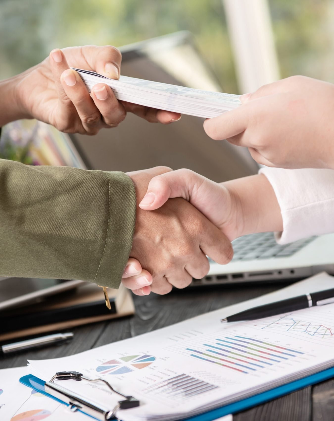 Business people shaking hands, finishing up meeting. businessman giving money to his partner while making contract - bribery and corruption concepts.